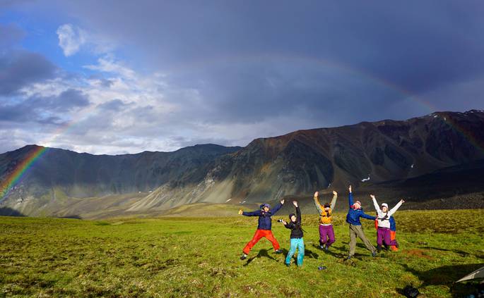 A group of students jumps in front of a rainbow in Alaska.