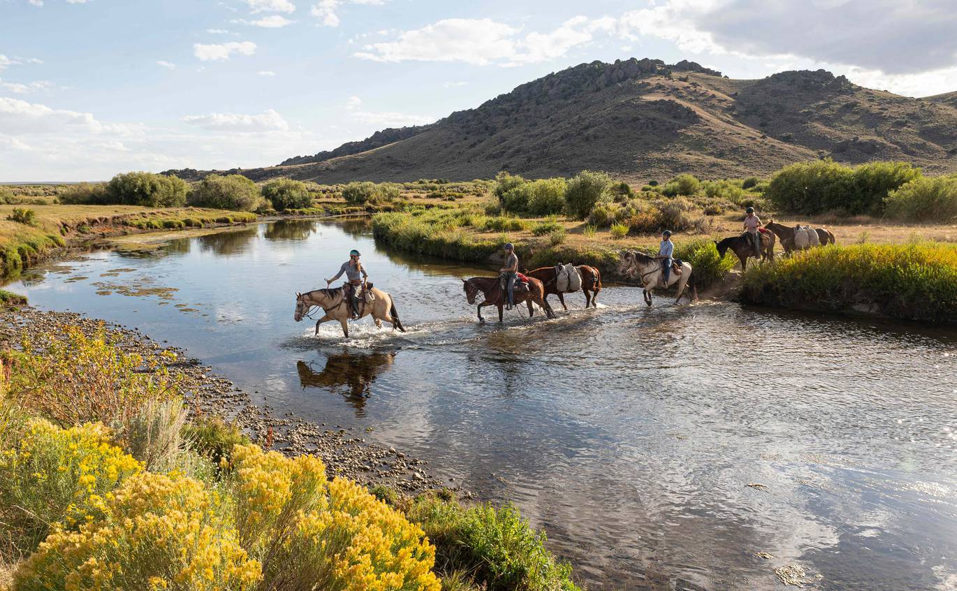 Four course participants crossing a river on horseback in Wyoming's backcountry.