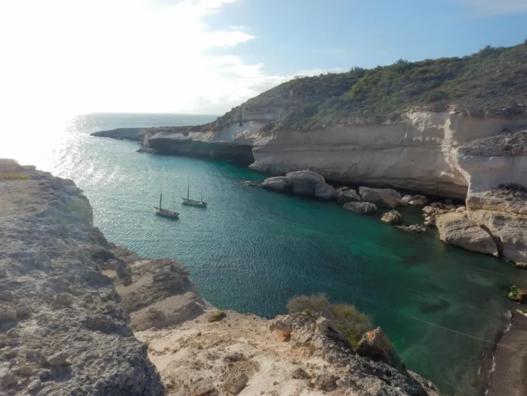 Sailboats anchored in a protected cove at sunset.