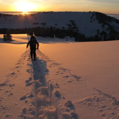 The sun dips behind the snow capped mountains as students ski across the snow.