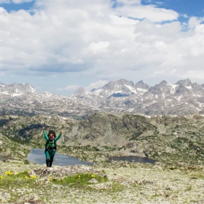 A course participant throws up their arms while backpacking in front of a spectacular view of the Wind River Range.