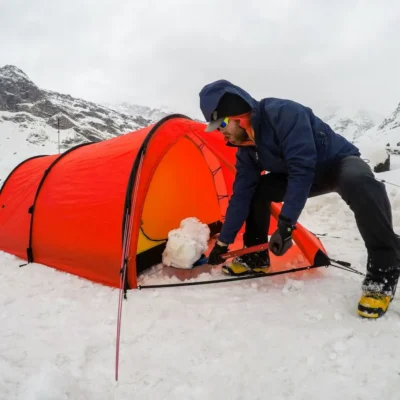 Student shoveling snow near the tent, in a weathered mountain region in India.