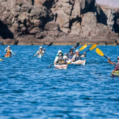 Students sea kayaking by rocky cliffs in the bright blue waters of Baja California, Mexico.