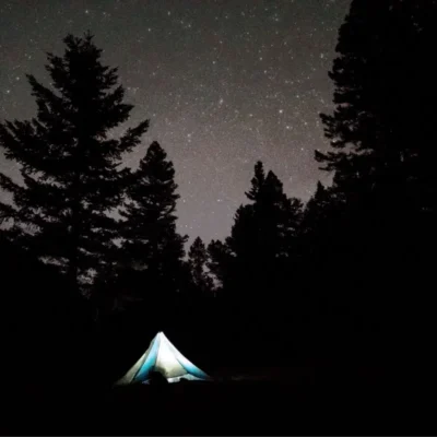 A headlamp illuminates a tent as the many stars shine.