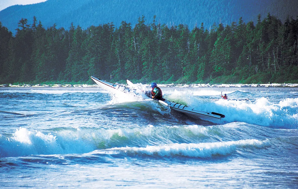 A course participant crests a large wave with a sea kayak in the waters of coastal British Columbia.