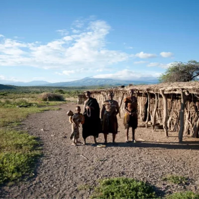 Group of East African locals smiles gleefully for a picture with a wide open field in the background.