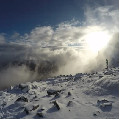 A student stands silhouetted on a snowy ridge amidst the clouds in Patagonia.