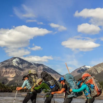 Course participants work together to cross a stream while backpacking in Alaska's Wrangell–St. Elias National Park and Preserve.