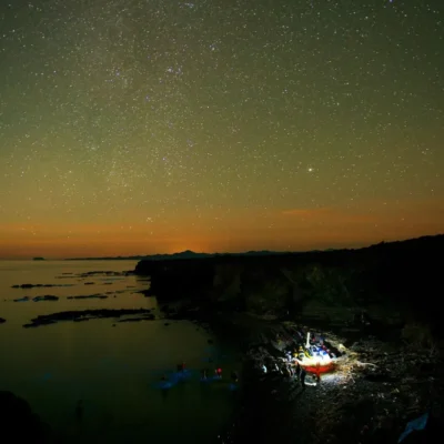 Nighttime view of camp on the beach in Mexico with sea kayaks lined up on the shore.