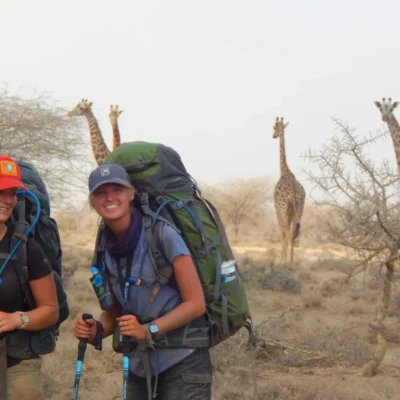 Students smile in front of giraffes while backpacking through Tanzania.