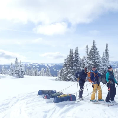 Students pulling sleds along the snowy terrain to a basecamp in the mountains.