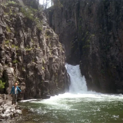 View of a gushing waterfall, as a student gleefully stands beside the shoreline.