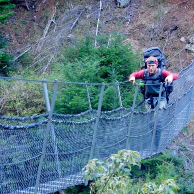 A student crosses a suspension bridge over a river in New Zealand.