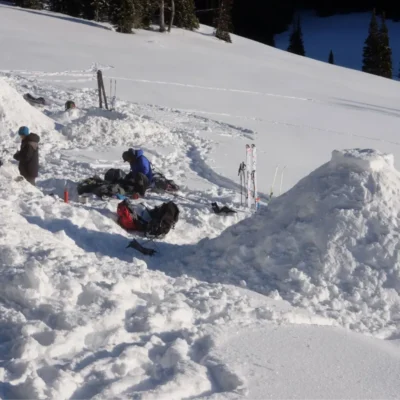 Students organizing gear near their snow shelters.