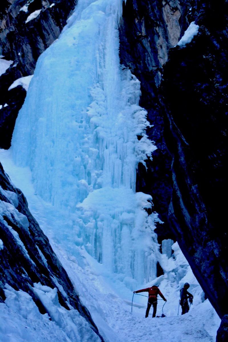 Two climbers coil a rope at the base of an ice waterfall