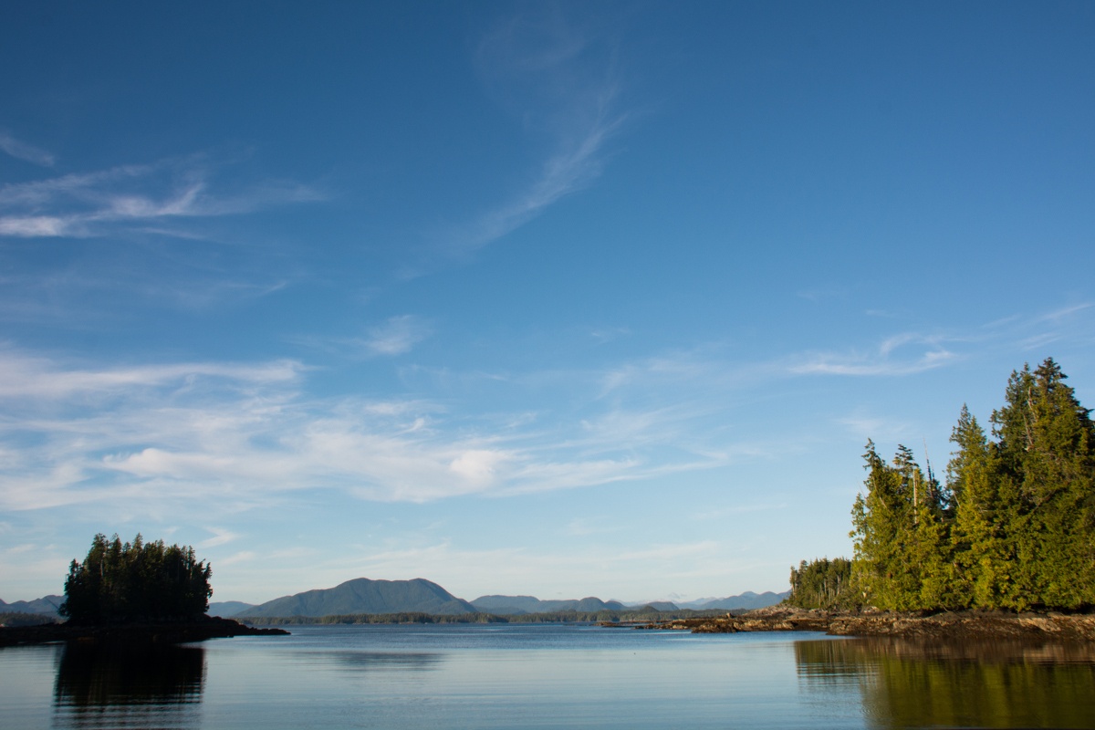 smooth blue water on a sunny day with thickly vegetated islands and mountains