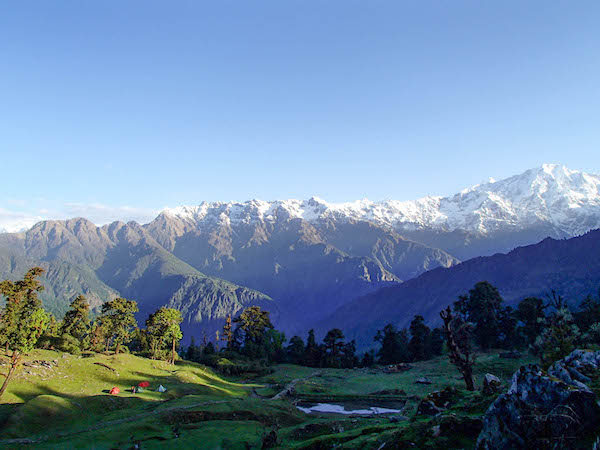 green valley in the Himalayas with NOLS tents and snow-capped mountains behind