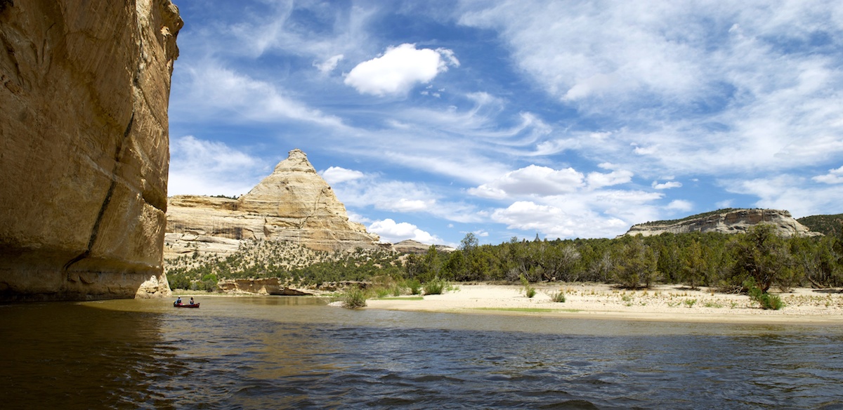 NOLS students paddle through Yampa Canyon on a sunny day with swirls of clouds above