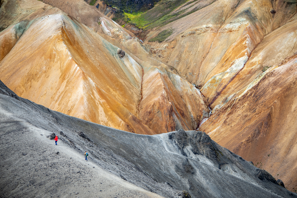 two hikers are walking on trail along a ridge. 