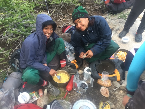 smiling C5 students smile while making backcountry mac and cheese on a NOLS course