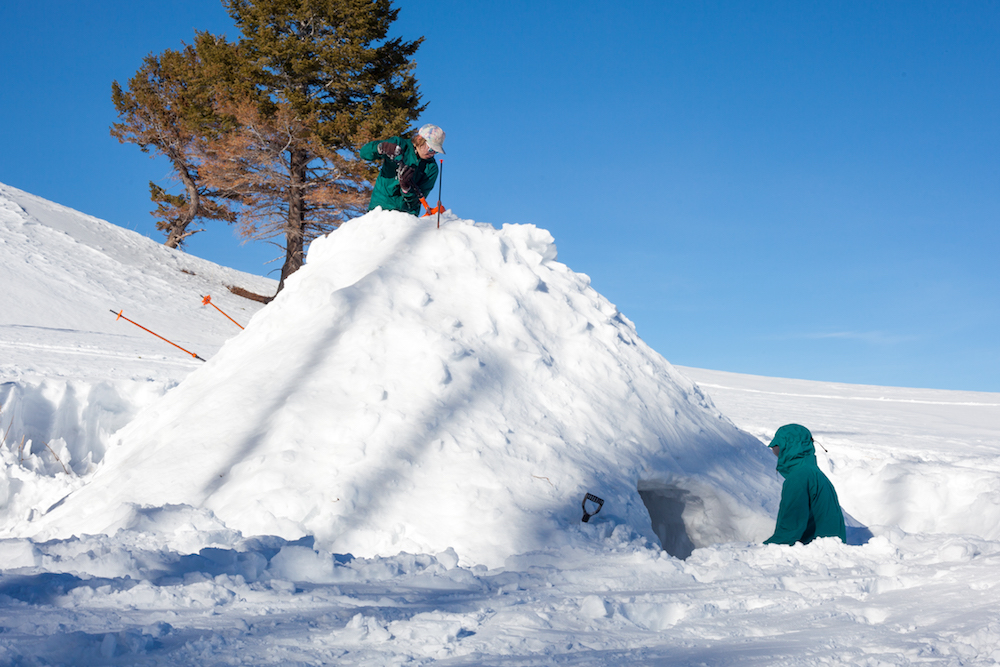 A camper climbs to the top of quinzhee to carve a vent for air