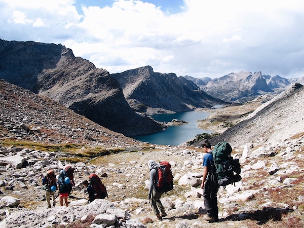 Five NOLS students descend a rocky slope toward alpine lakes in the Rockies