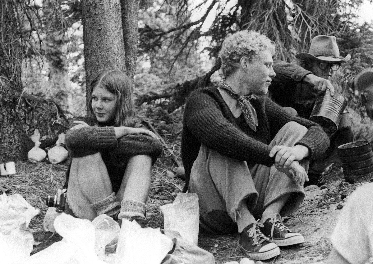 black and white photo of several NOLS students taking a break on an expedition in the 1970s with one student pouring liquid out of a billycan
