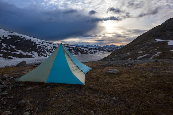 blue and tan tent in Scandinavia at sunset with water and snow dusted mountains nearby