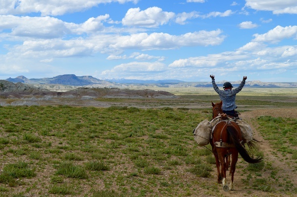 NOLS horsepacking student raises arms on horseback while traveling in the Wyoming backcountry
