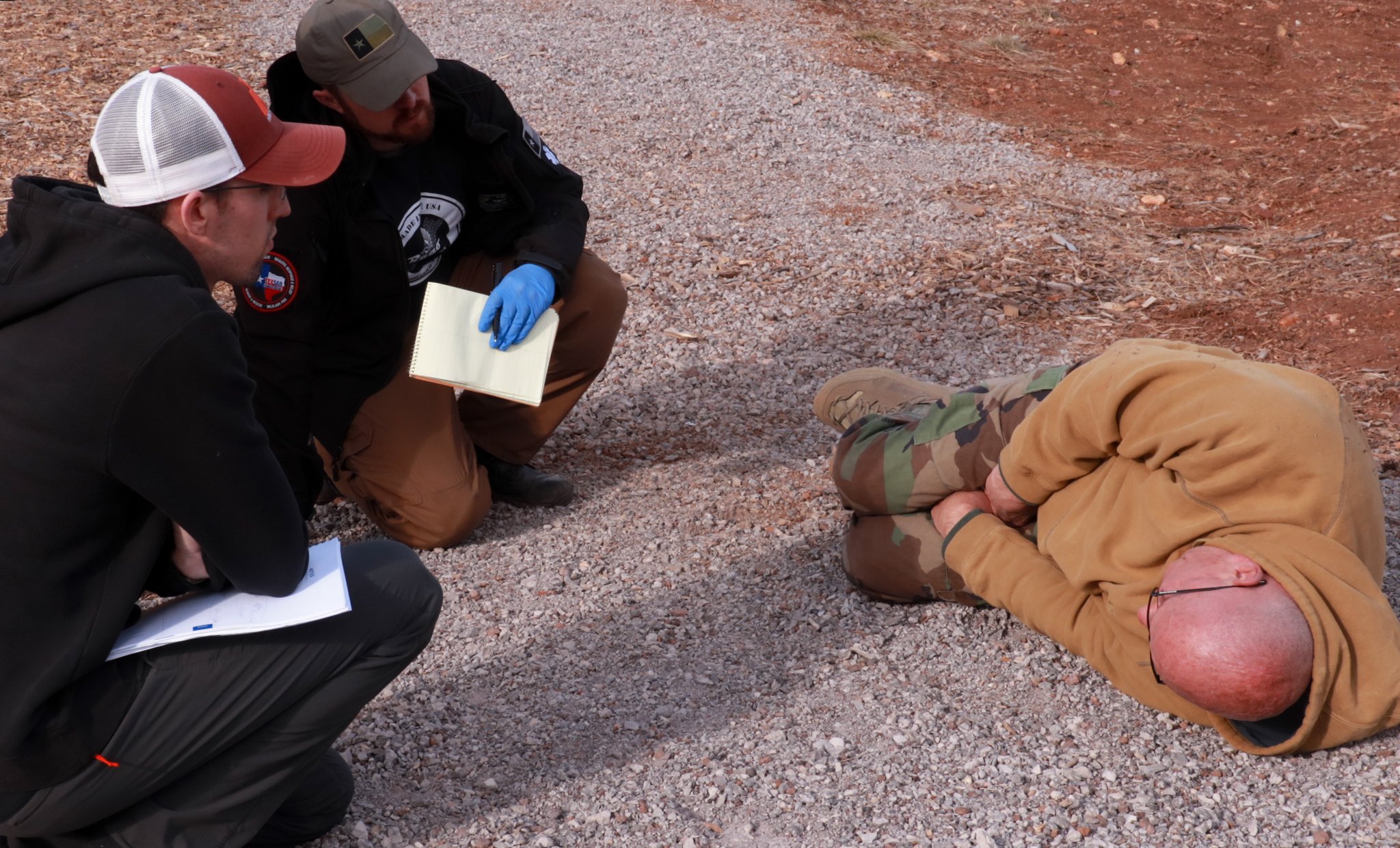 Two male rescuers carrying note pads evaluate an older bald male patient.