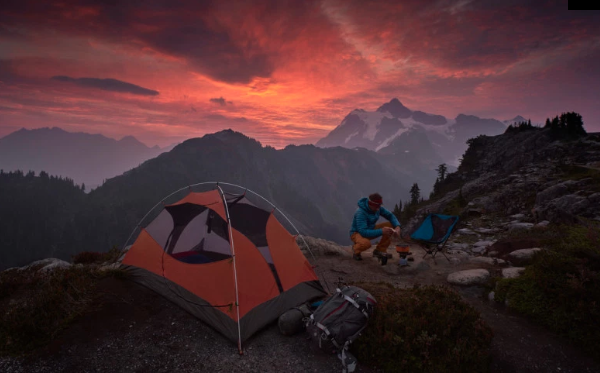 tent beside a man making a fire while camping in the mountains at sunset