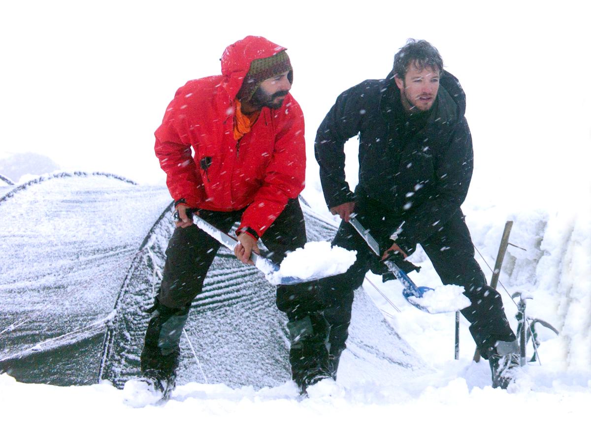 NOLS participants shovel snow outside a tent to stay warm