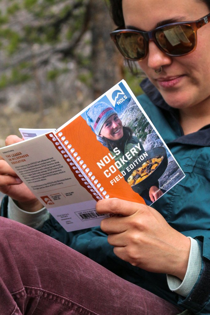 Woman reads the spiral-bound NOLS Cookery book