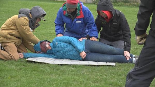 three Wilderness First Aid students kneel beside a "patient" in a scenario