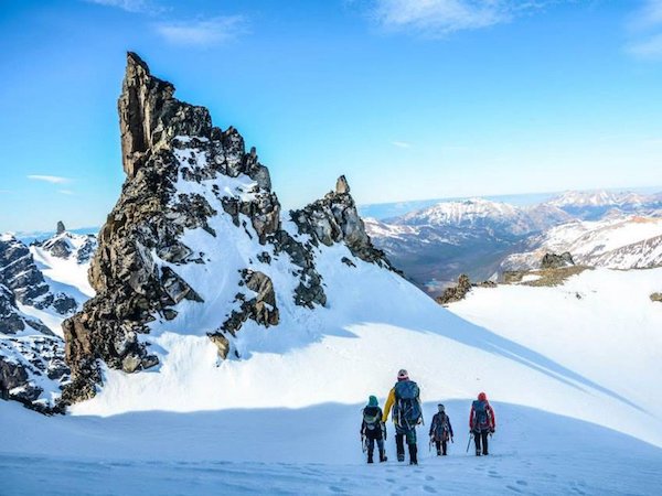 four NOLS participants trek across a snowfield toward crag in Patagonia's mountains