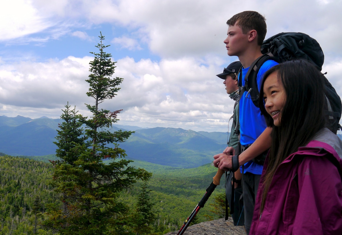 NOLS students smile and look over green mountain ridge