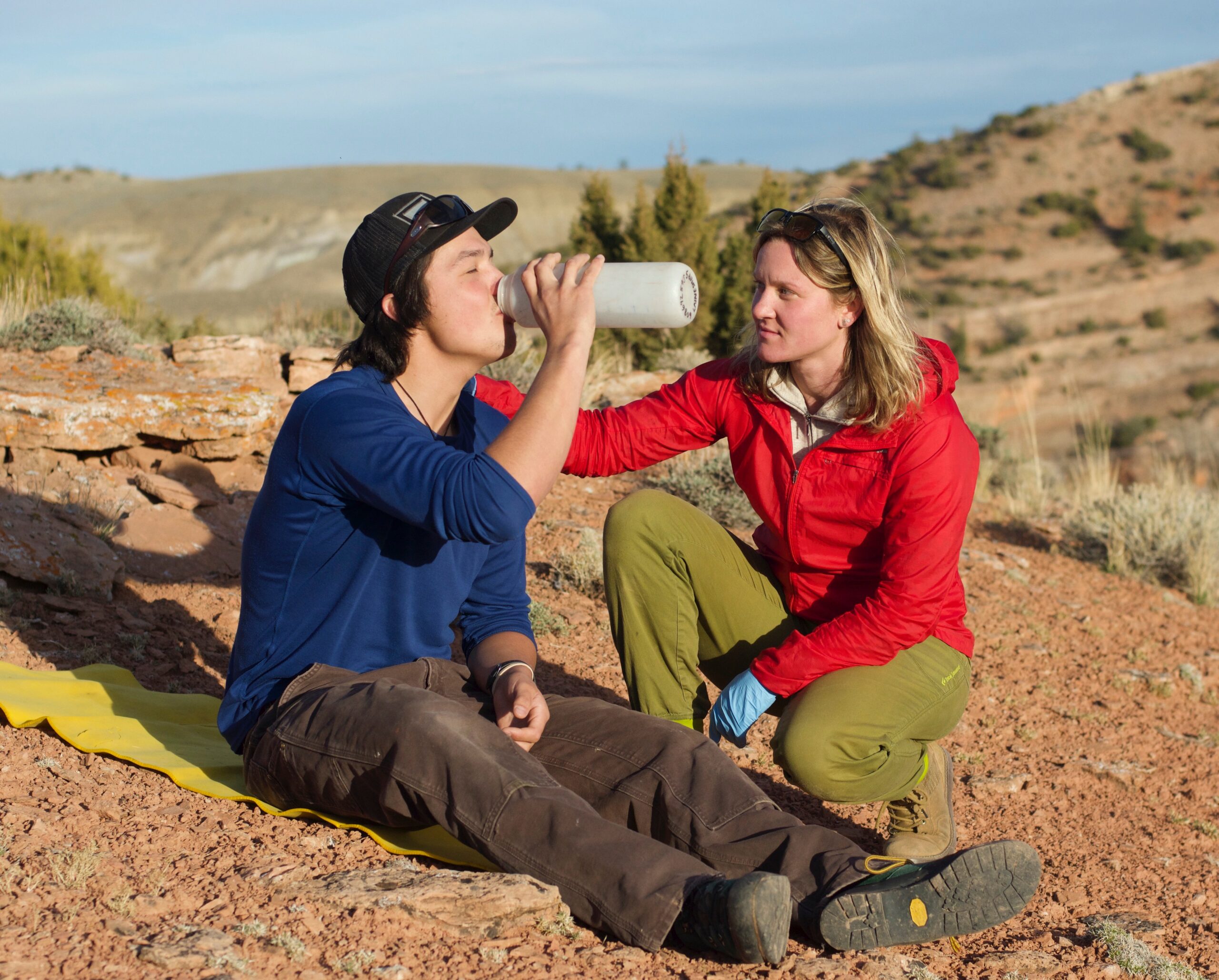 NOLS wilderness medicine participant puts a hand on the shoulder of a mock patient drinking water