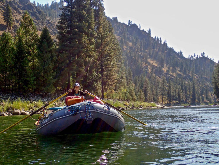Teen girl with a big smile on her face on a raft solo holding the oars floating down river
