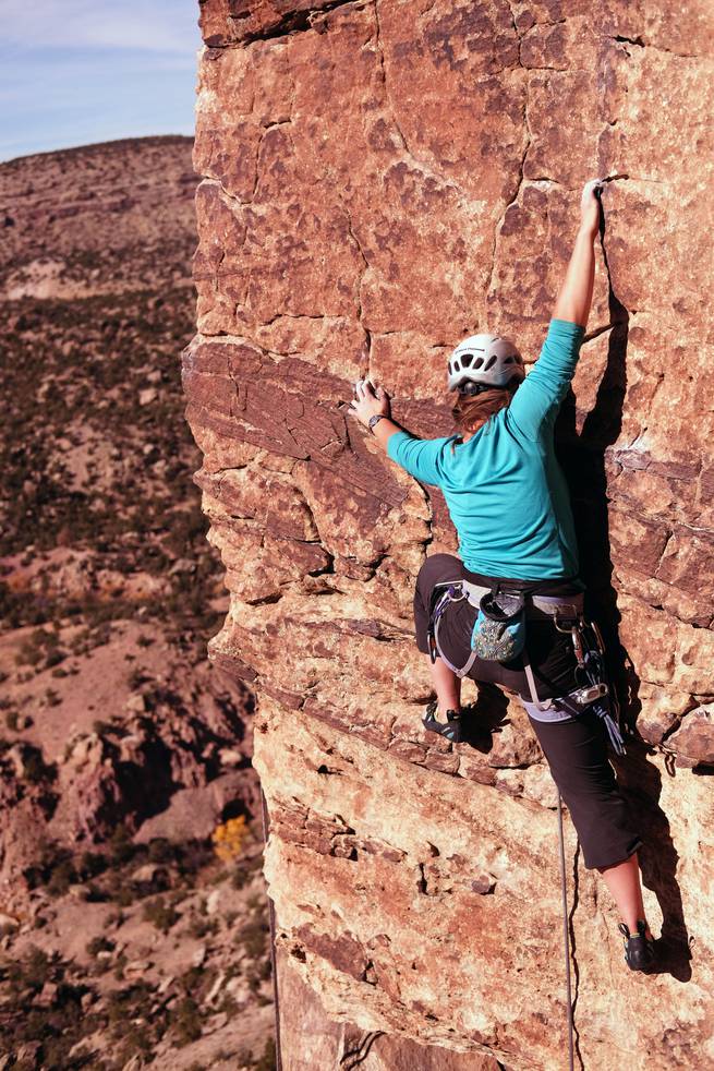 Student free climbing a cliff face with chalked hands