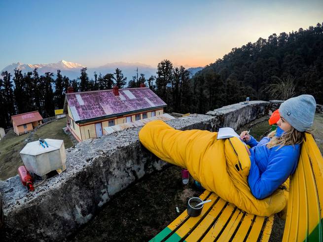 A student journals in their sleeping bag at sunset while looking out at India's Kumaon Himalaya.