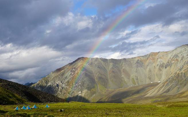 Rainbow in Alaska's Talkeetna Mountains with cluster of NOLS tents nearby.