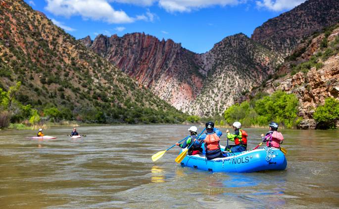 Course participants paddle in a raft and on kayaks on the river
