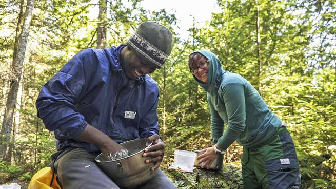 A student and an instructor laugh together while making dough for cinnamon rolls.