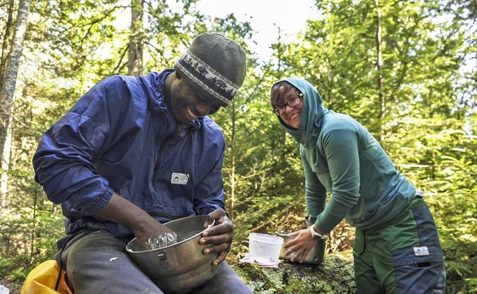 A student and an instructor laugh together while making dough for cinnamon rolls.