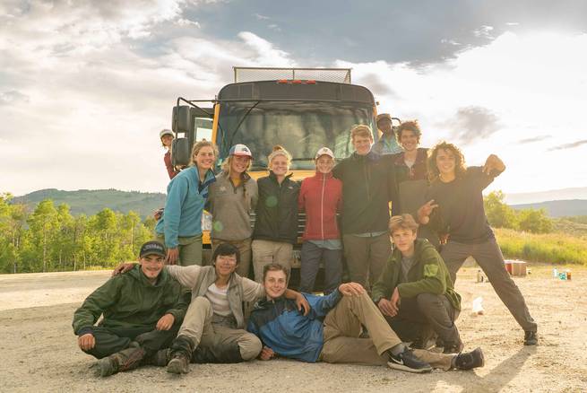 Students smile for a group photo in front of a school bus before heading into the Wind River Wilderness.