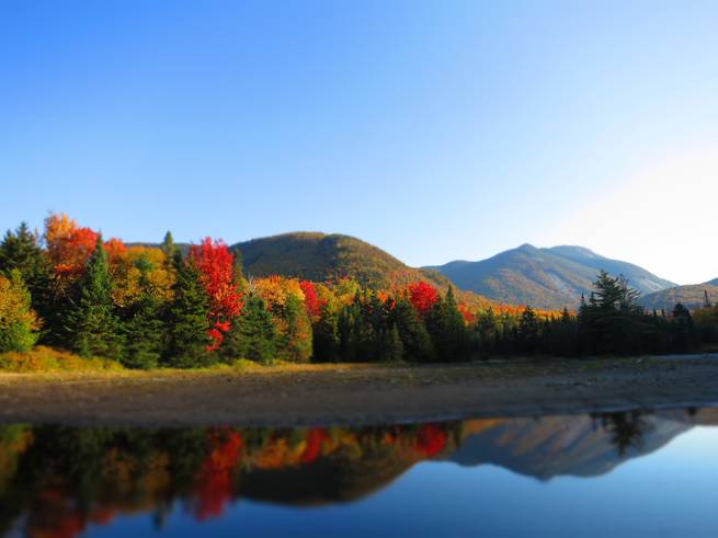 The vibrant colors of fall foliage are reflected in the glassy surface of a lake in the Adirondacks.