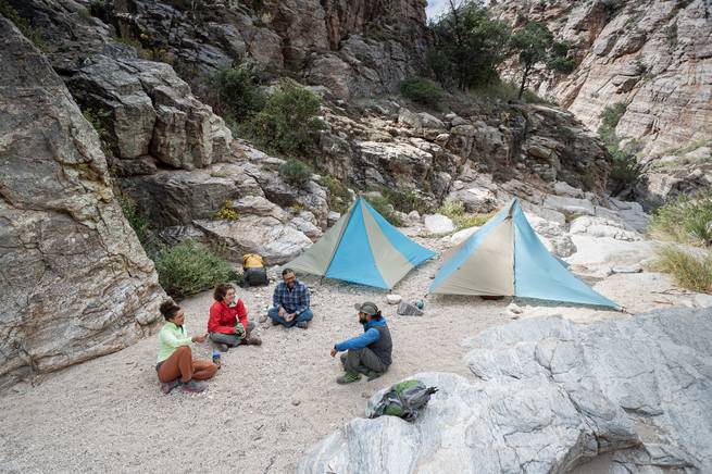 4 people camping between cliffs with two tents set up