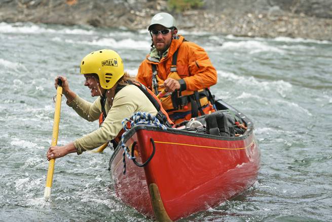 A smiling student demonstrates a cross bow draw while whitewater canoeing in the Yukon.