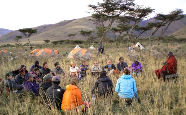 Students sitting in a circle listen to a local villager in Tanzania.
