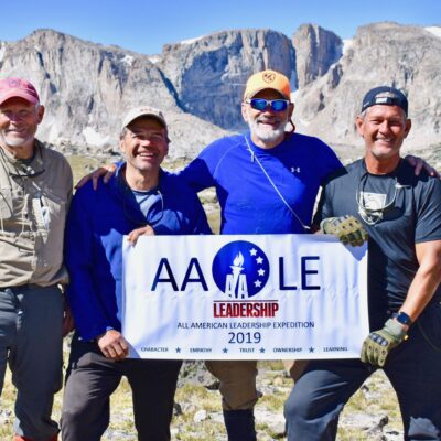 Course participants pose together with the AALE banner in front of rugged peaks of the Wind River Range.
